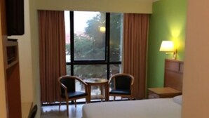 Una habitación de hotel con una cama, dos sillas, una mesita, una lámpara y una ventana con cortinas.