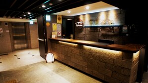 A reception area with a wooden counter, a wall-mounted sign, and an elevator. - FORTUNE INN (Taipei)
