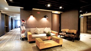 A modern lobby with a sofa, chairs, a coffee table, and magazines on a rack. - FORTUNE INN (Taipei)