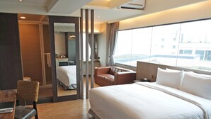 A hotel room with a large bed, a desk, a chair, a mirror, and a view of the city. - FORTUNE INN (Taipei)