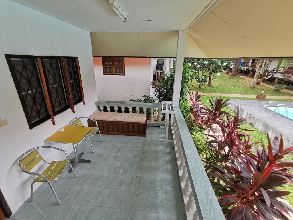 Un espace extérieur abrité, équipé d’une table et de chaises, d’un banc, et offrant une vue sur un jardin avec des plantes et une piscine.