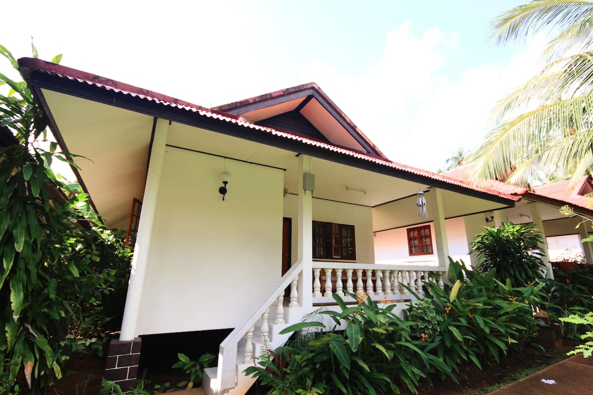 A two-story house with a balcony, surrounded by lush greenery.