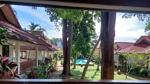 A view from a balcony overlooking a courtyard with a swimming pool, surrounded by trees and buildings with red roofs. - Fullmoon House Samui (Koh Samui)