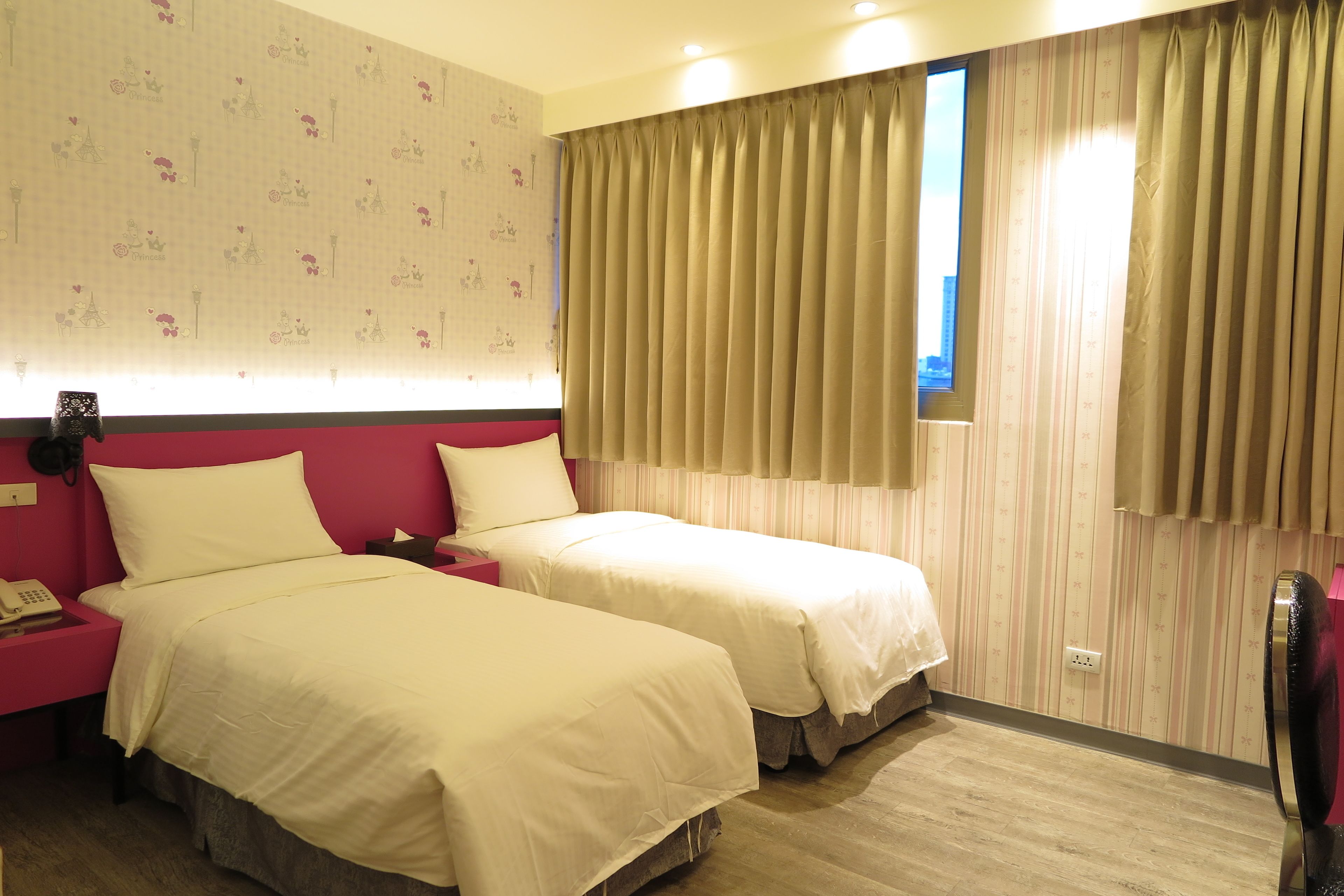 A hotel room with two beds, a nightstand with a phone, and a window with curtains.