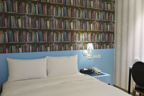 A hotel room with a large bookshelf filled with books, a bed with white linens, a bedside table with a lamp, and a chair. - 191 Hotel (Taoyuan City)