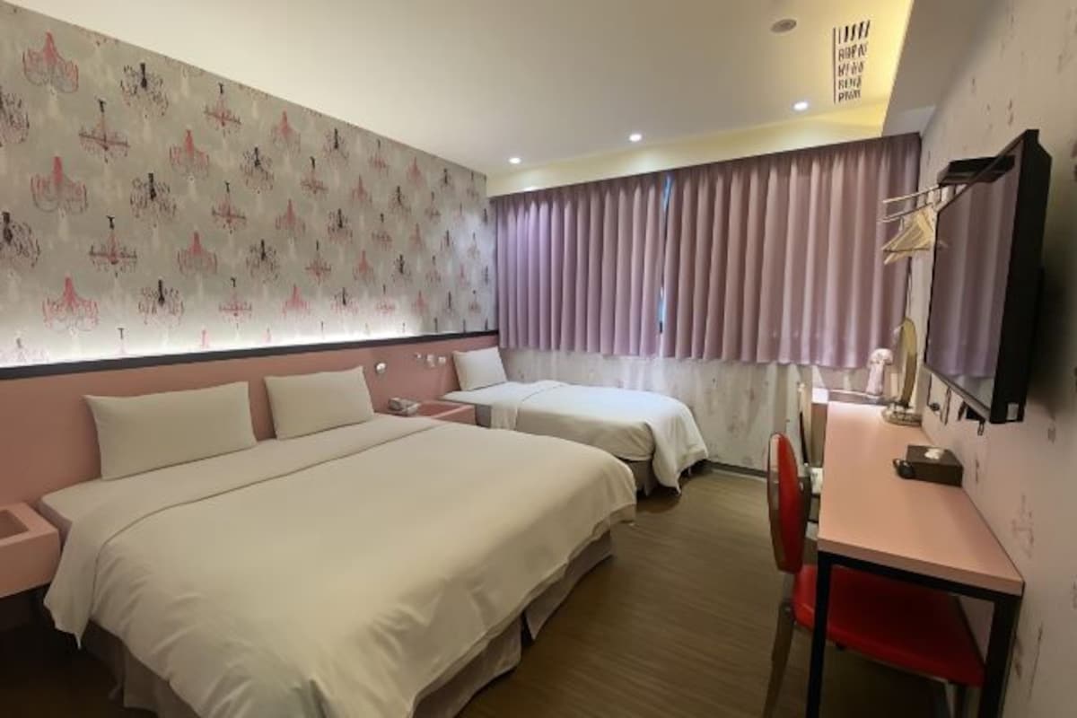 A hotel room with two beds, a desk, and a chair.