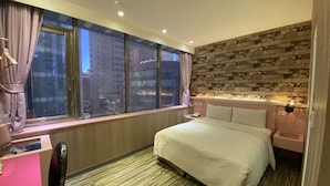 A hotel room with a large window, a bed, a desk, and a chair.