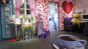 A hotel lobby with a Christmas theme, including a large teddy bear, a heart-shaped floral arrangement, and a cup of hot chocolate.