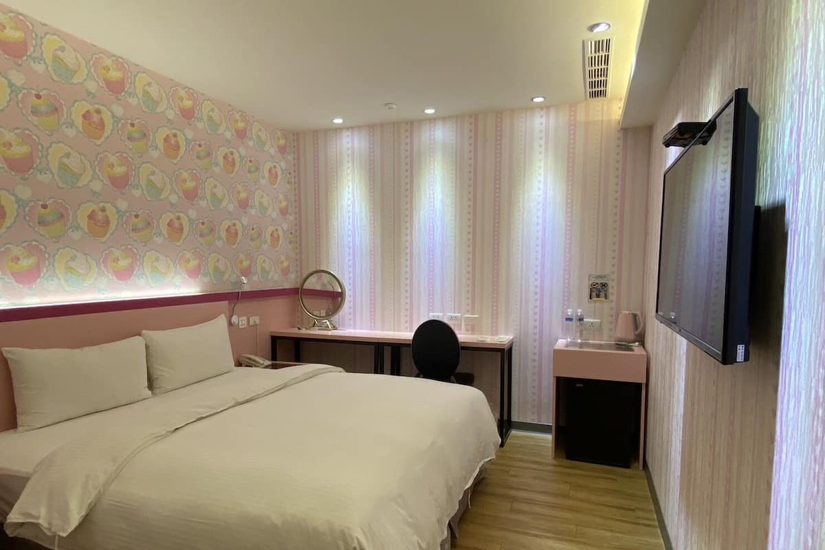 A hotel room with a large bed, a desk, a chair, a TV, and a bathroom.