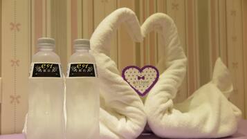 Dos botellas con etiquetas y un arreglo de toallas con forma de corazón y diseño de lazo.