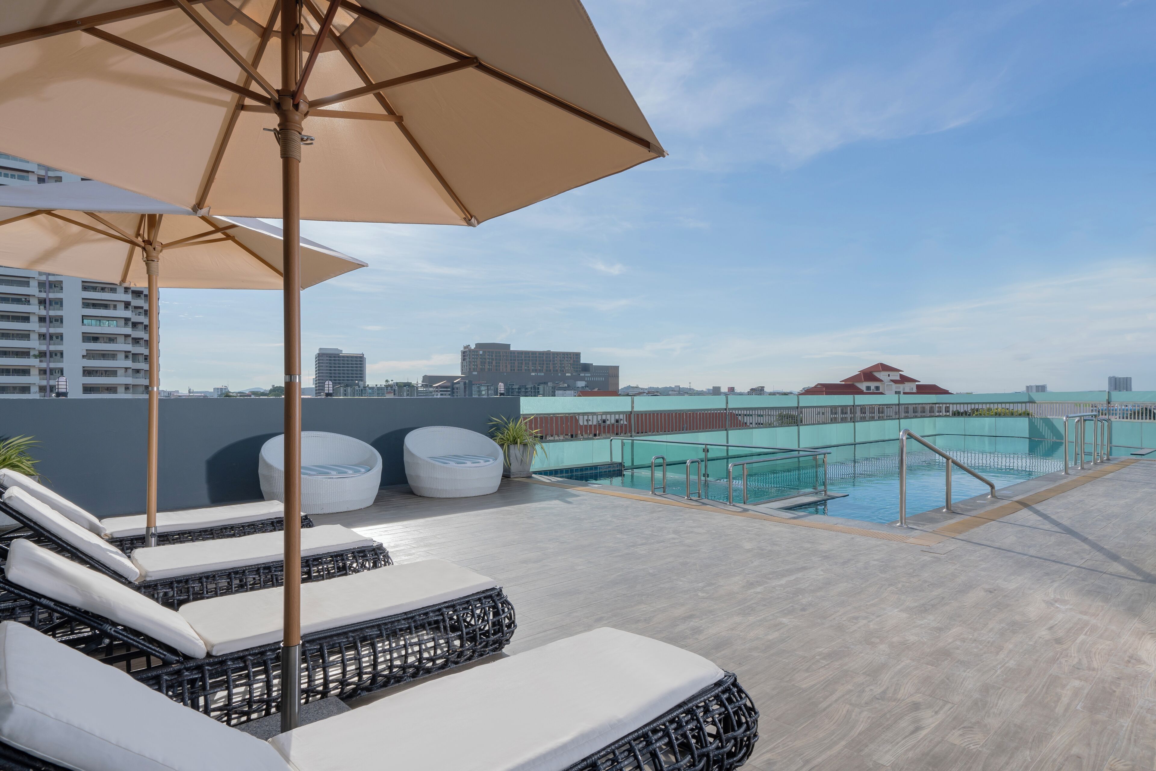 Uma área de piscina no terraço com espreguiçadeiras e guarda-sóis, piscina e vista para a cidade.