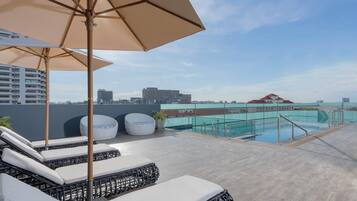 A rooftop pool area with lounge chairs and umbrellas, a pool, and a cityscape view.