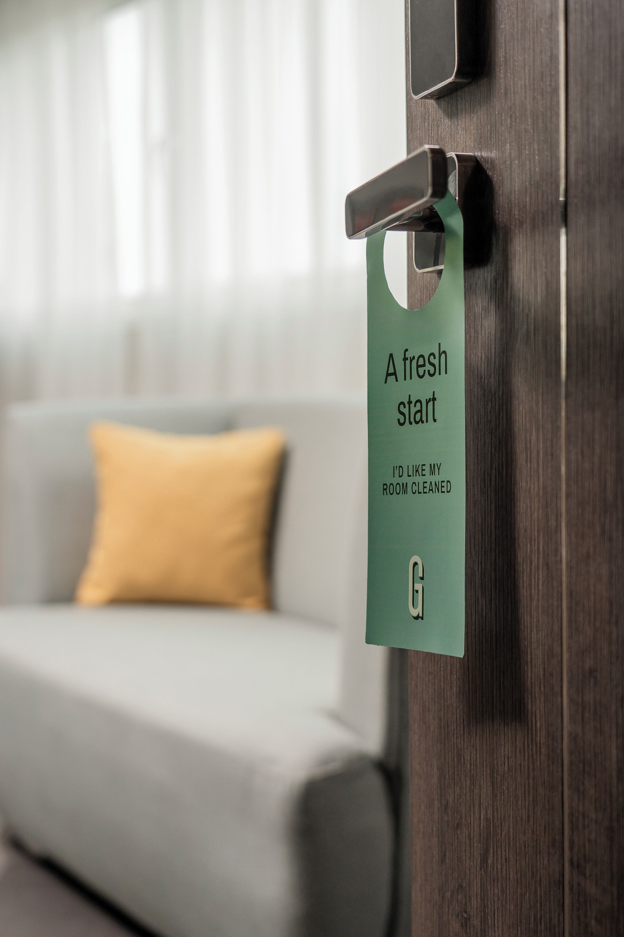 Puerta de una habitación de hotel con un cartel que anuncia un nuevo comienzo y solicita servicio de limpieza.