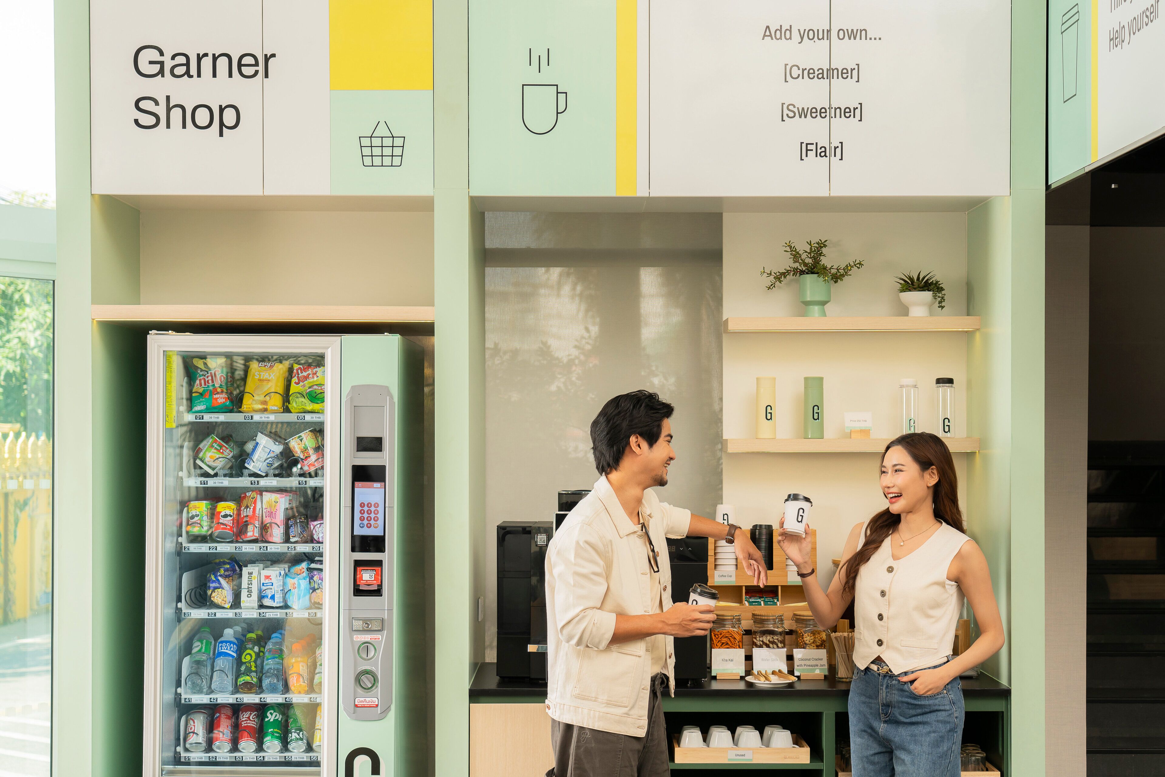 Un homme et une femme se trouvent dans un magasin, devant un distributeur automatique, avec des étagères remplies de produits et une enseigne au-dessus des étagères.