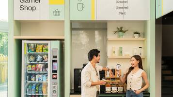 Un homme et une femme se trouvent dans un magasin, devant un distributeur automatique, avec des étagères remplies de produits et une enseigne au-dessus des étagères.