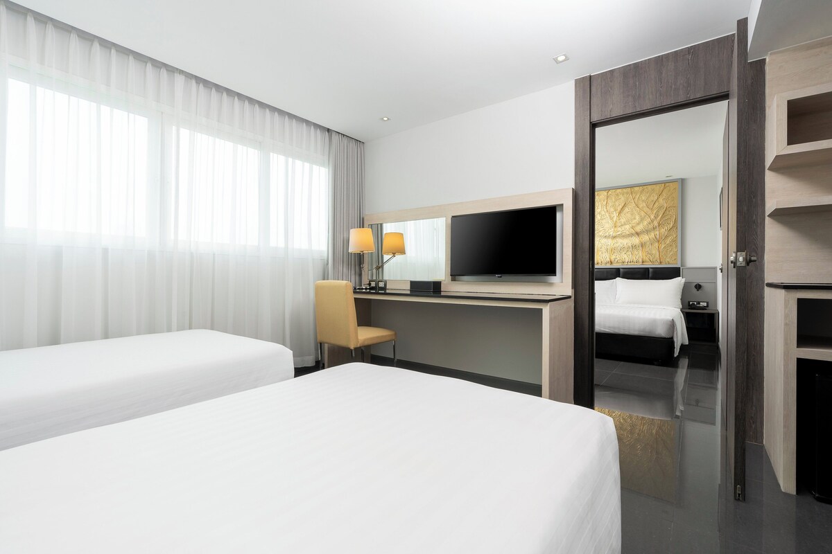 Una habitación de hotel con dos camas, un escritorio con televisor y un espejo grande.