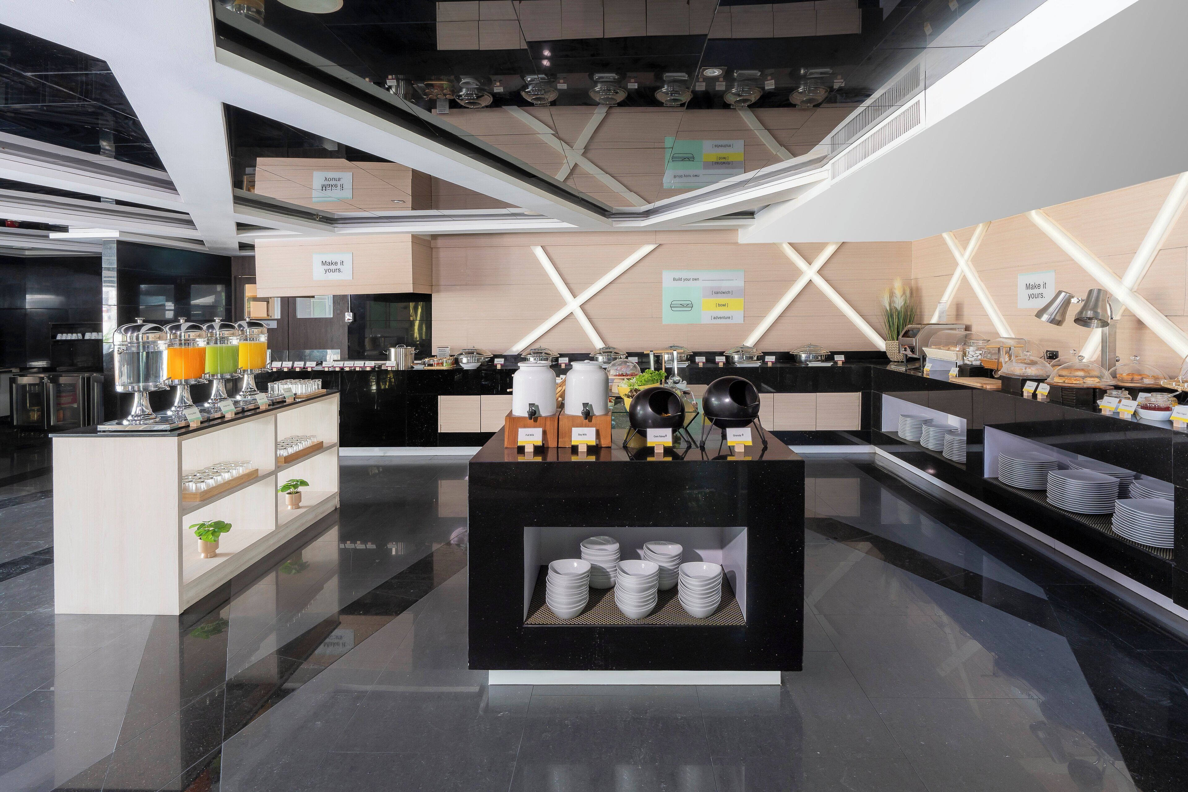 Un hall d’hôtel moderne avec un comptoir d’accueil central, un espace où l’on peut se servir du café et un coin salon offrant une vue sur le hall.