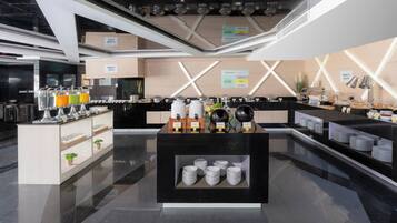 Un hall d’hôtel moderne avec un comptoir d’accueil central, un espace où l’on peut se servir du café et un coin salon offrant une vue sur le hall.