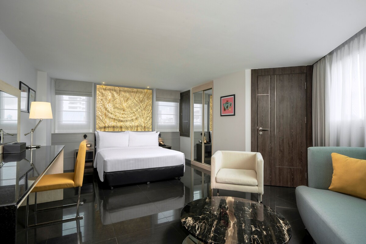 Una habitación de hotel moderna con una cama, un escritorio, una silla, un sofá y un espejo grande.