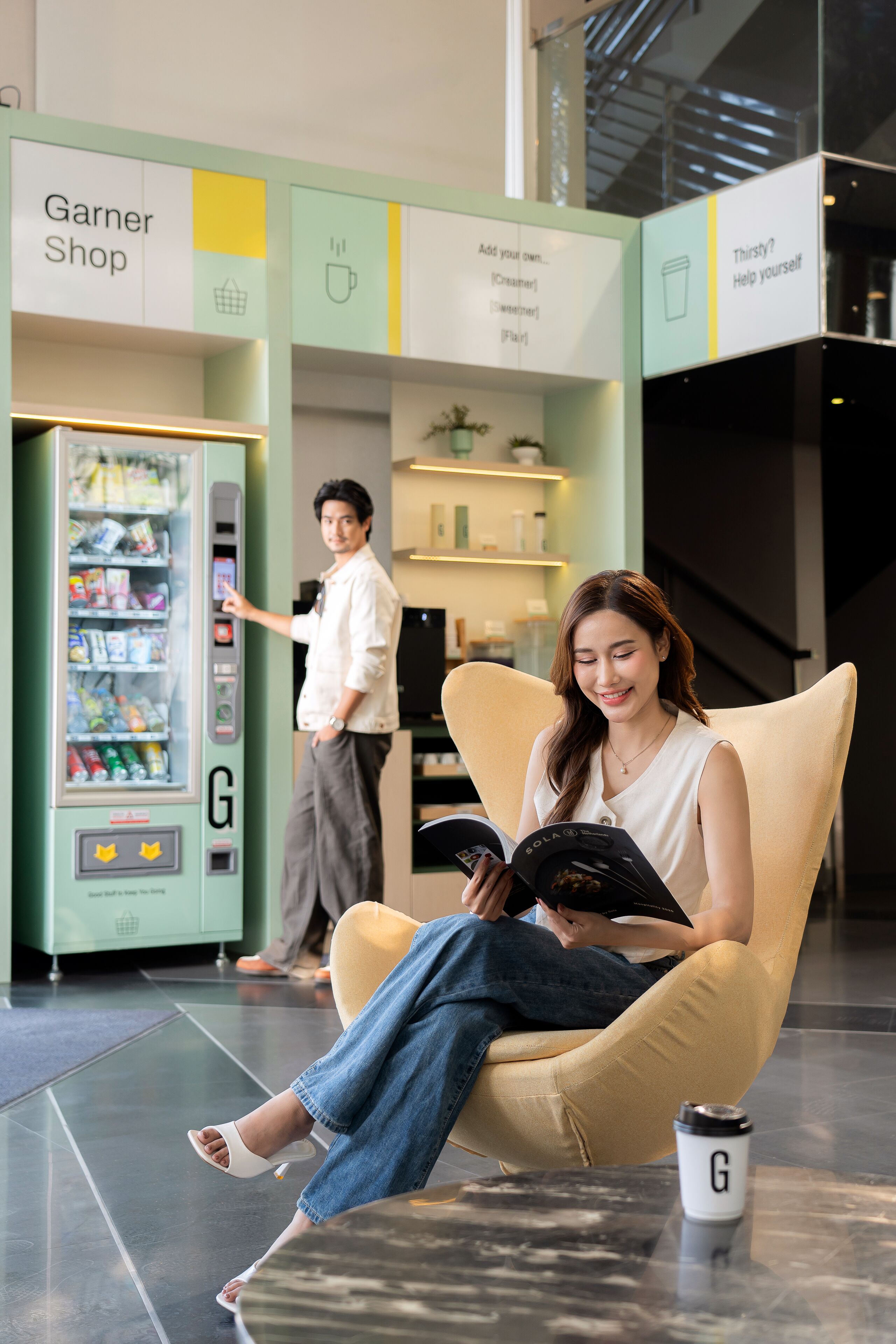 A modern interior with a vending machine labeled 'Garner Shop,' a seating area, and a coffee cup on a table.