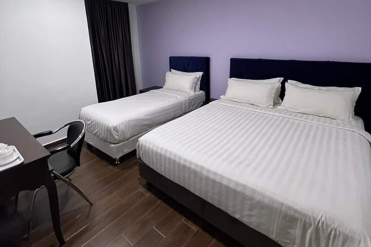 A hotel room with two single beds, a desk with a chair, and a dark-colored headboard.