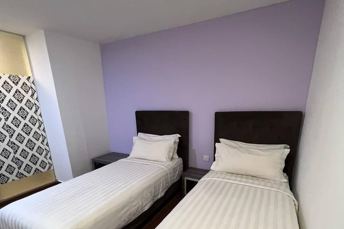 Two single beds with dark headboards and white bedding in a room with a purple wall and wooden flooring.