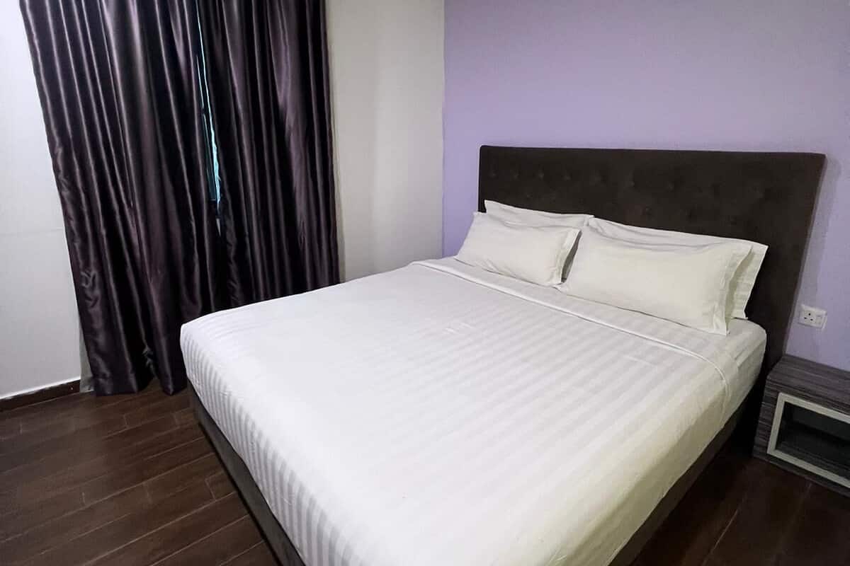 A neatly made bed in a room with a dark wooden floor and a purple wall.