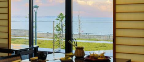 Une table à manger, dressée avec des plats, et une vue sur la mer par de grandes fenêtres.