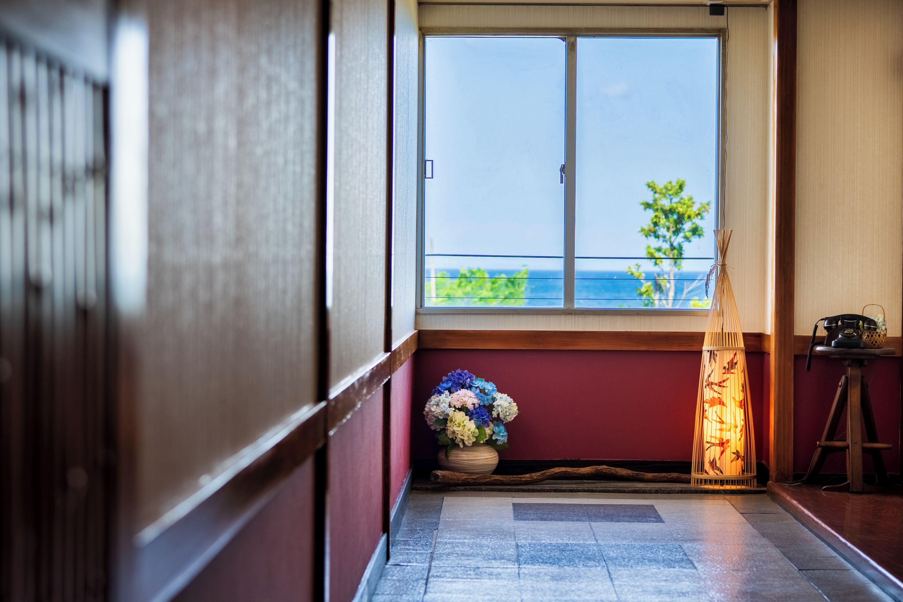 Una stanza con vista sul mare, pavimento in legno, un tavolino con una lampada e un vaso con fiori.