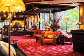 Un vestíbulo de hotel con asientos, una alfombra estampada en rojo y arreglos florales.