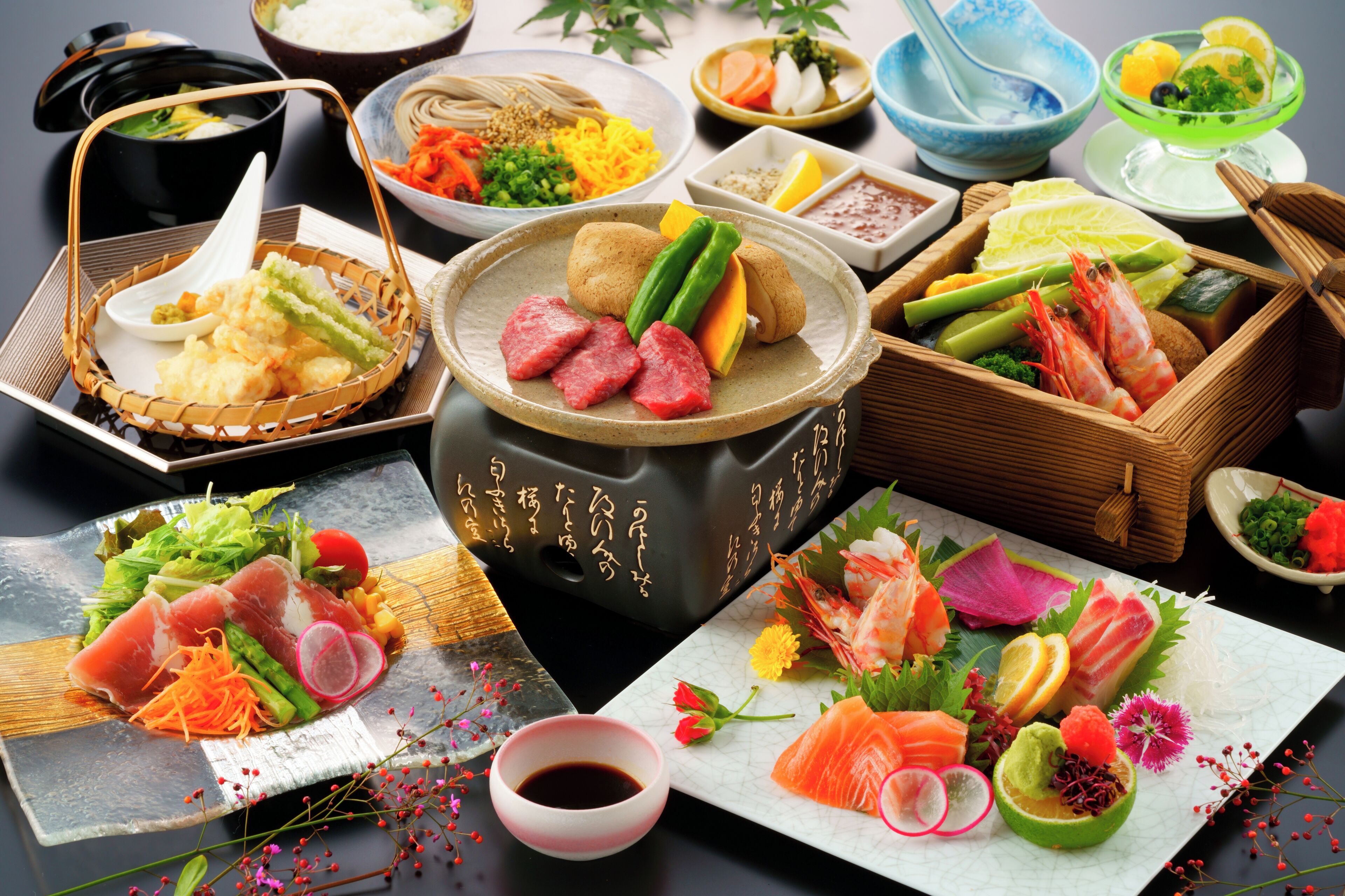 A variety of Japanese dishes including sushi, sashimi, and tempura, arranged on a table with multiple serving dishes and a hot pot.