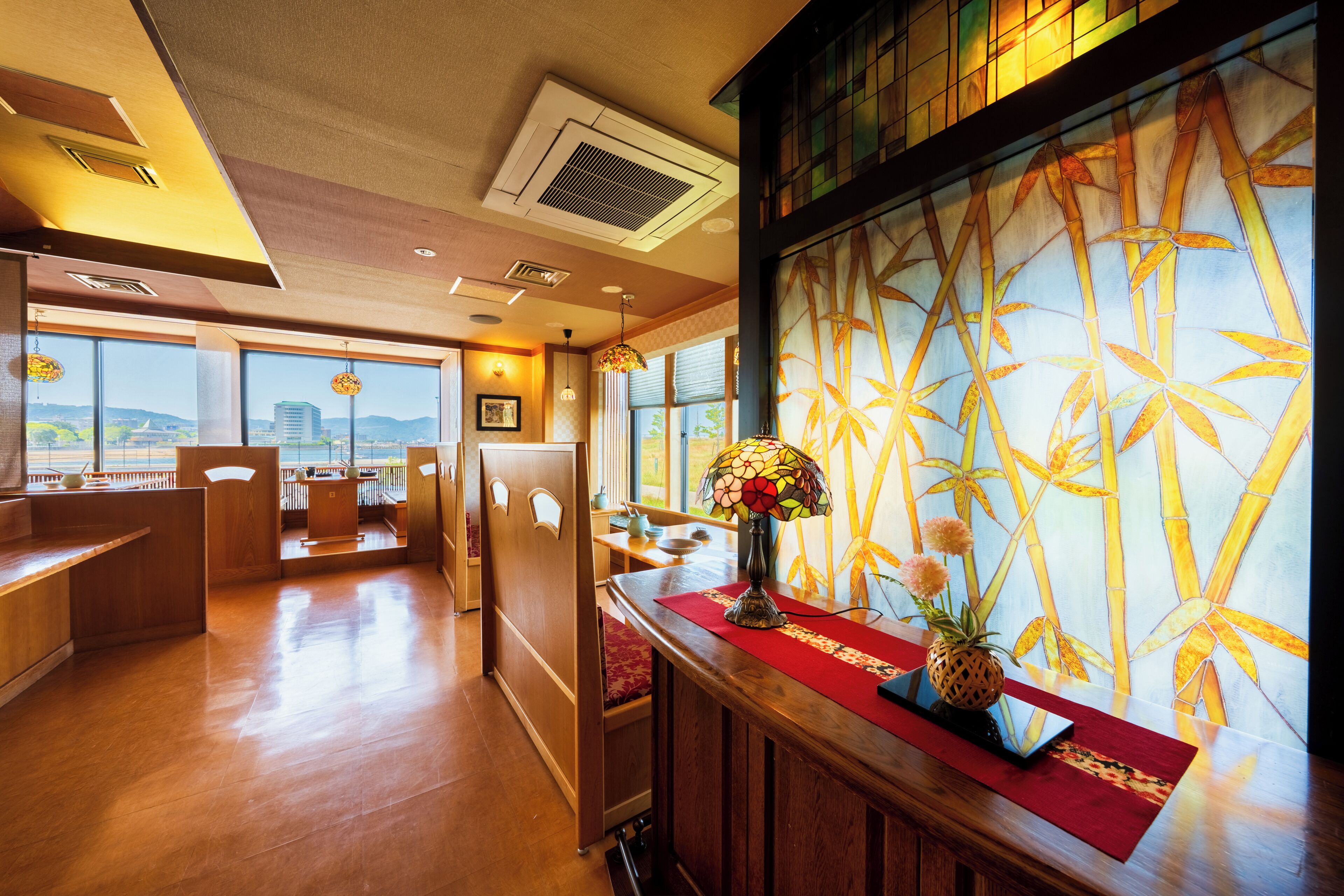 A hotel lobby with a wooden reception desk, a red runner, and a large window with a view of the city.