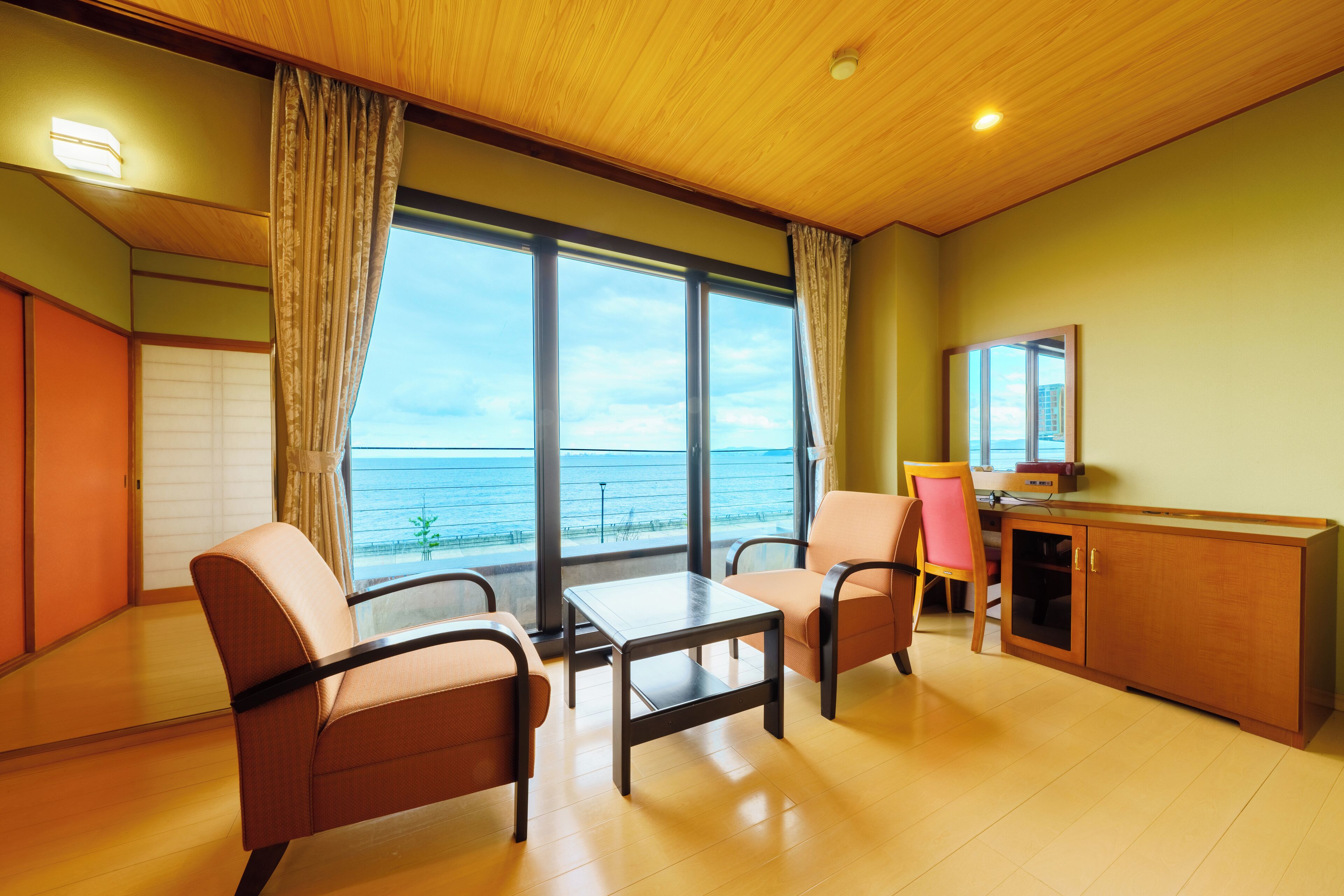 A room with a wooden ceiling, large windows with curtains, a desk, two chairs, and a cabinet.