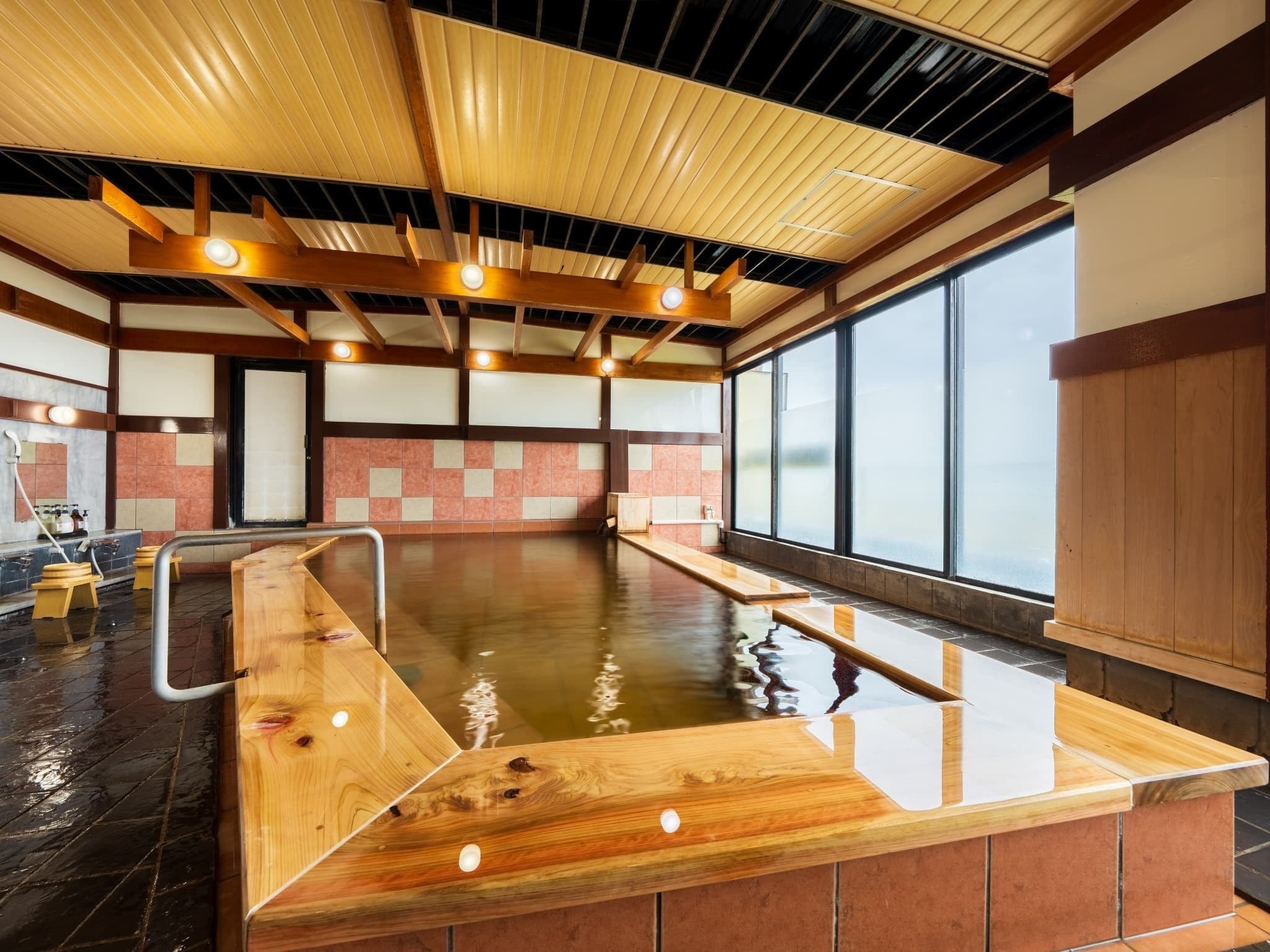 A modern indoor swimming pool with wooden benches and a tiled floor.