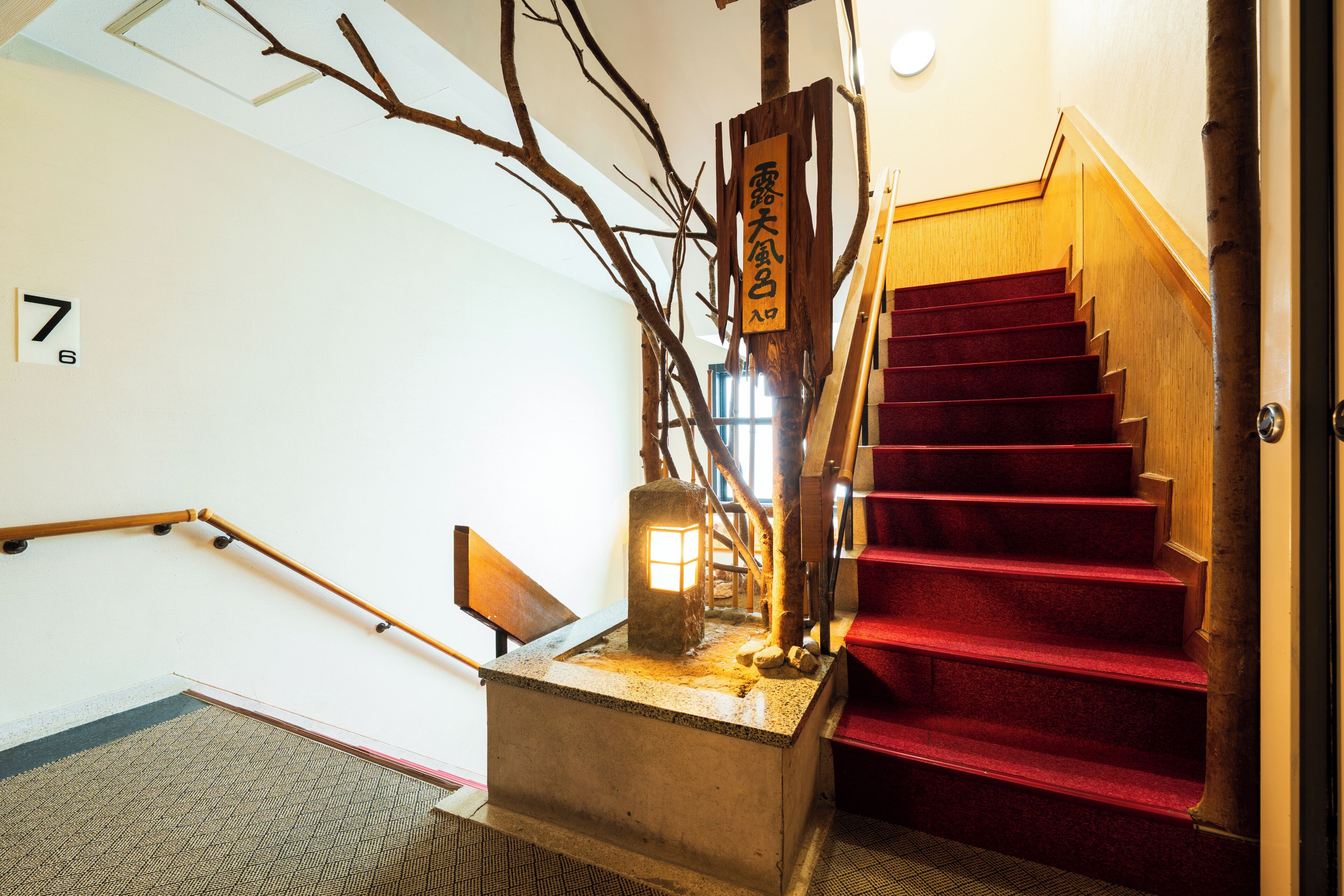 A staircase with a wooden handrail, a red carpeted landing, and a lantern.