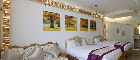 A hotel room with two beds, a sofa, a small table with a vase and a bicycle, and a wall with three autumn-themed paintings.