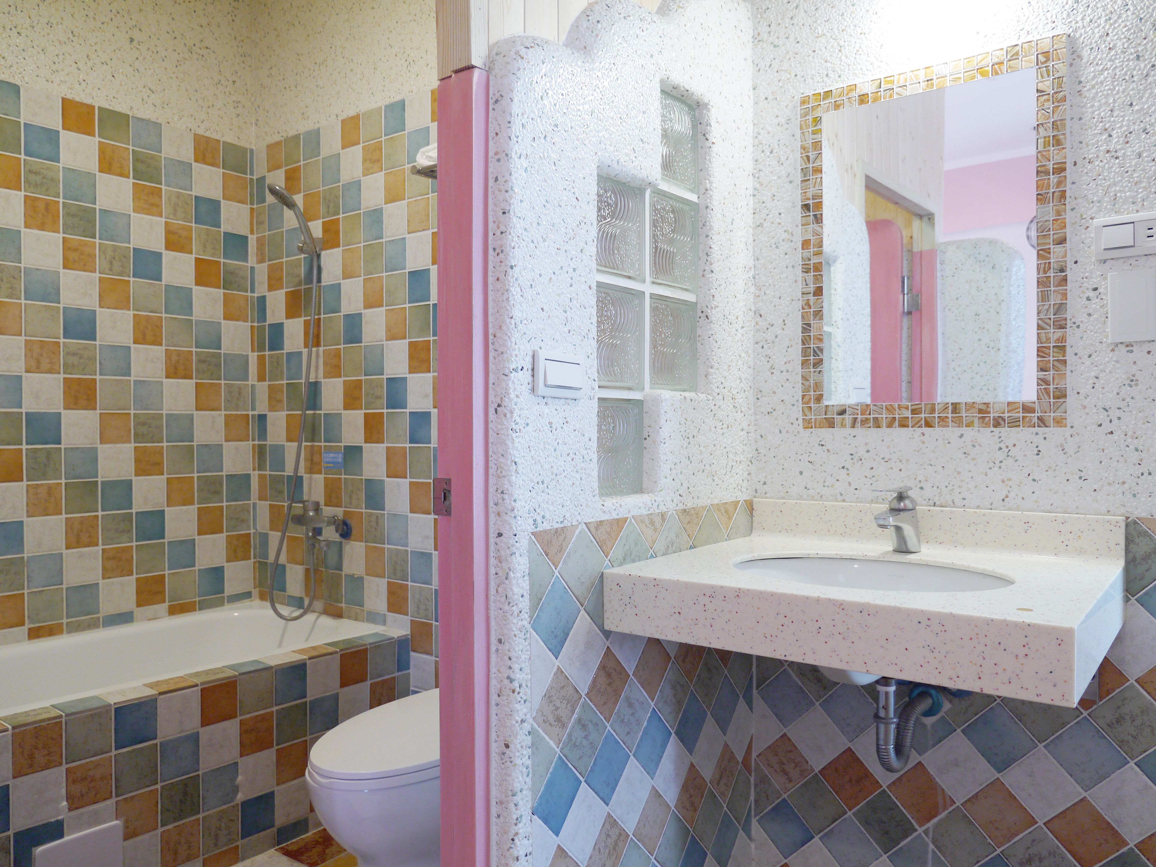 A bathroom with a tiled shower, a toilet, and a sink with a mirror.