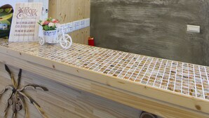 A wooden interior with a reception desk, a mounted television, a decorative wall with shelves, and a small refrigerator. - Sin Sin Hotel III (Hengchun)