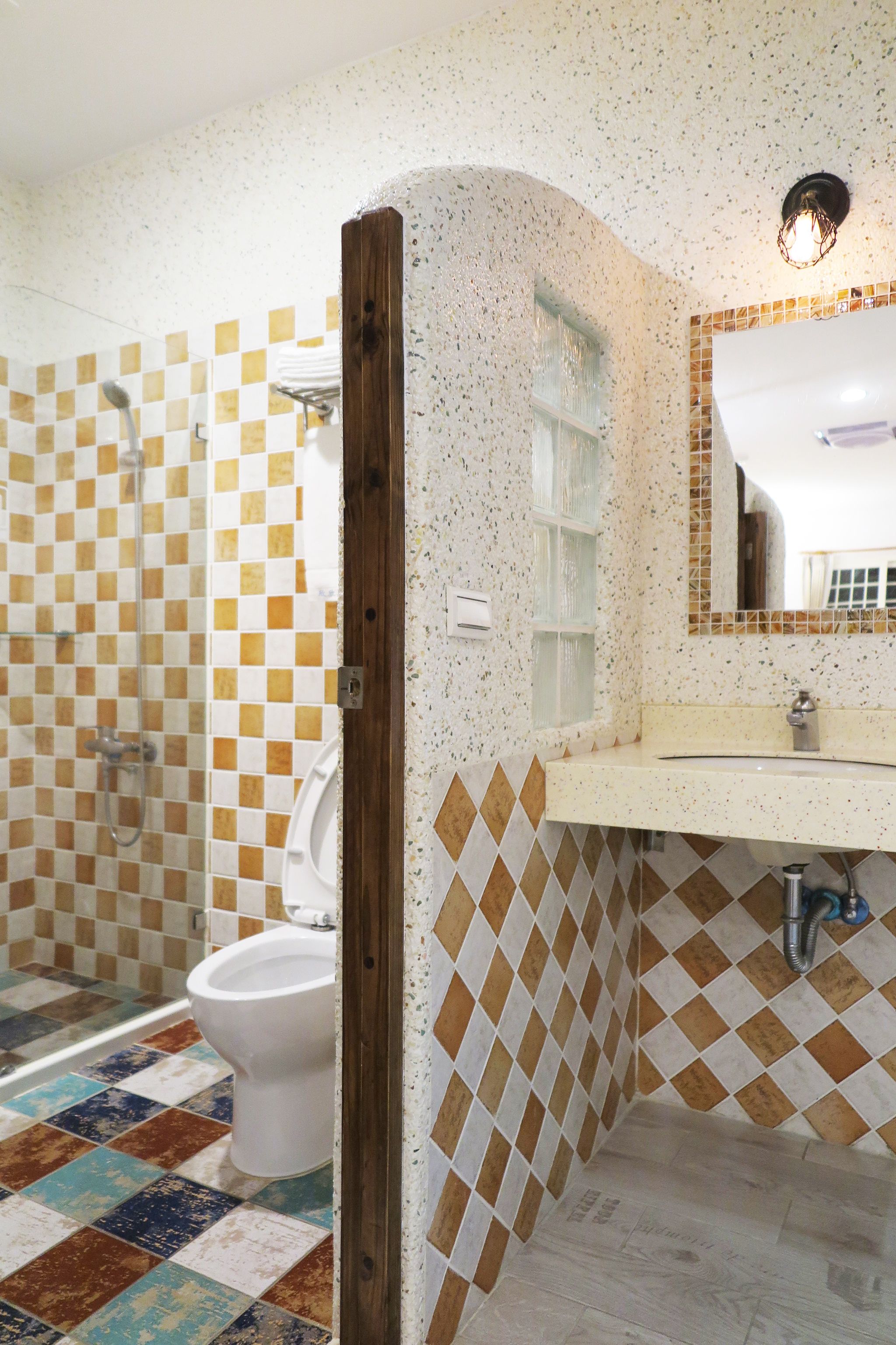 A bathroom with a checkered floor, a toilet, a shower, and a sink with a mirror above it.