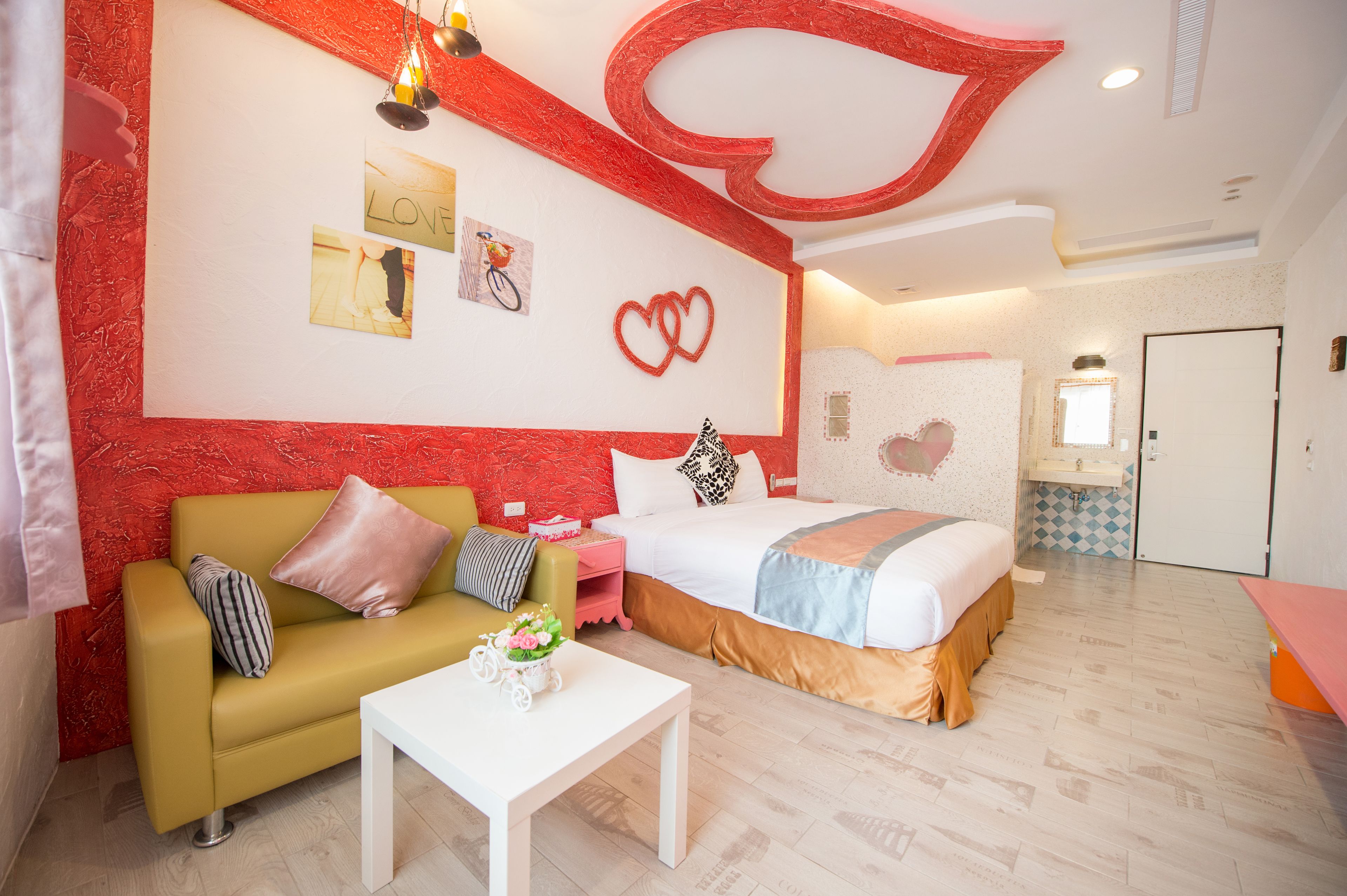 A modern hotel room with a large bed, a sofa, a small table, and a bathroom visible in the background.