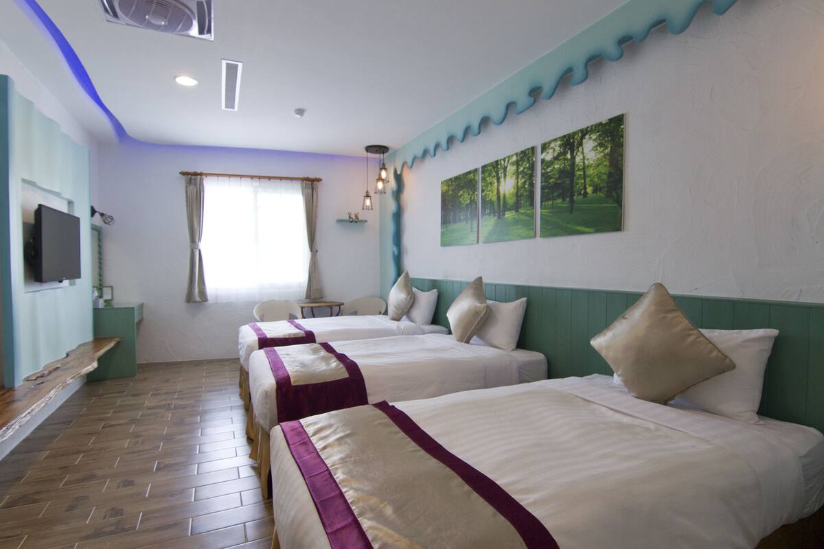 A hotel room with three beds, a television, a window with curtains, and a painting of a forest.
