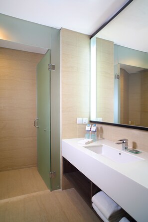 A modern bathroom with a glass shower enclosure, a white sink, and a large mirror. - Hotel Santika Premiere ICE - BSD City (Pagedangan)