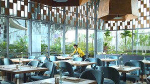Un restaurante moderno con una distribución limpia y ordenada, con sillas azules y mesas de madera, y grandes ventanales que ofrecen vistas al exterior.