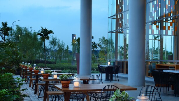 Un espacio para comer al aire libre con mesas y sillas de madera, rodeado de plantas en macetas y velas.