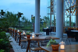 An outdoor dining area with wooden tables and chairs, surrounded by potted plants and candles. - Hotel Santika Premiere ICE - BSD City (Pagedangan)