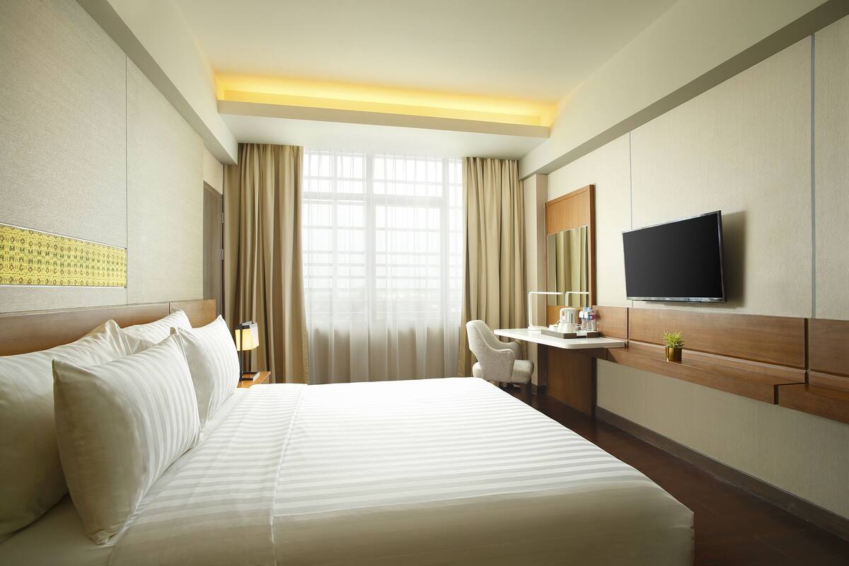 A hotel room with a large bed, a desk, a chair, a television, and a window with curtains.