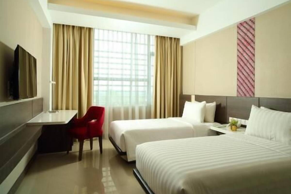 A hotel room with two beds, a desk, a chair, a TV, and a window with curtains.
