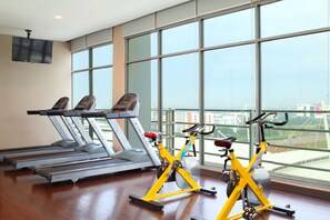 A gym with treadmills, stationary bikes, and a TV on the wall. - Hotel Santika Premiere ICE - BSD City (Pagedangan)