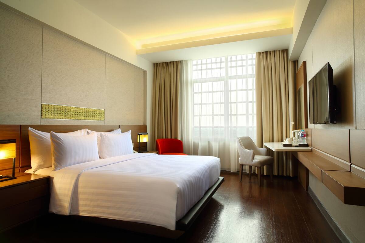 A hotel room with a large bed, a desk, a chair, and a television on the wall.