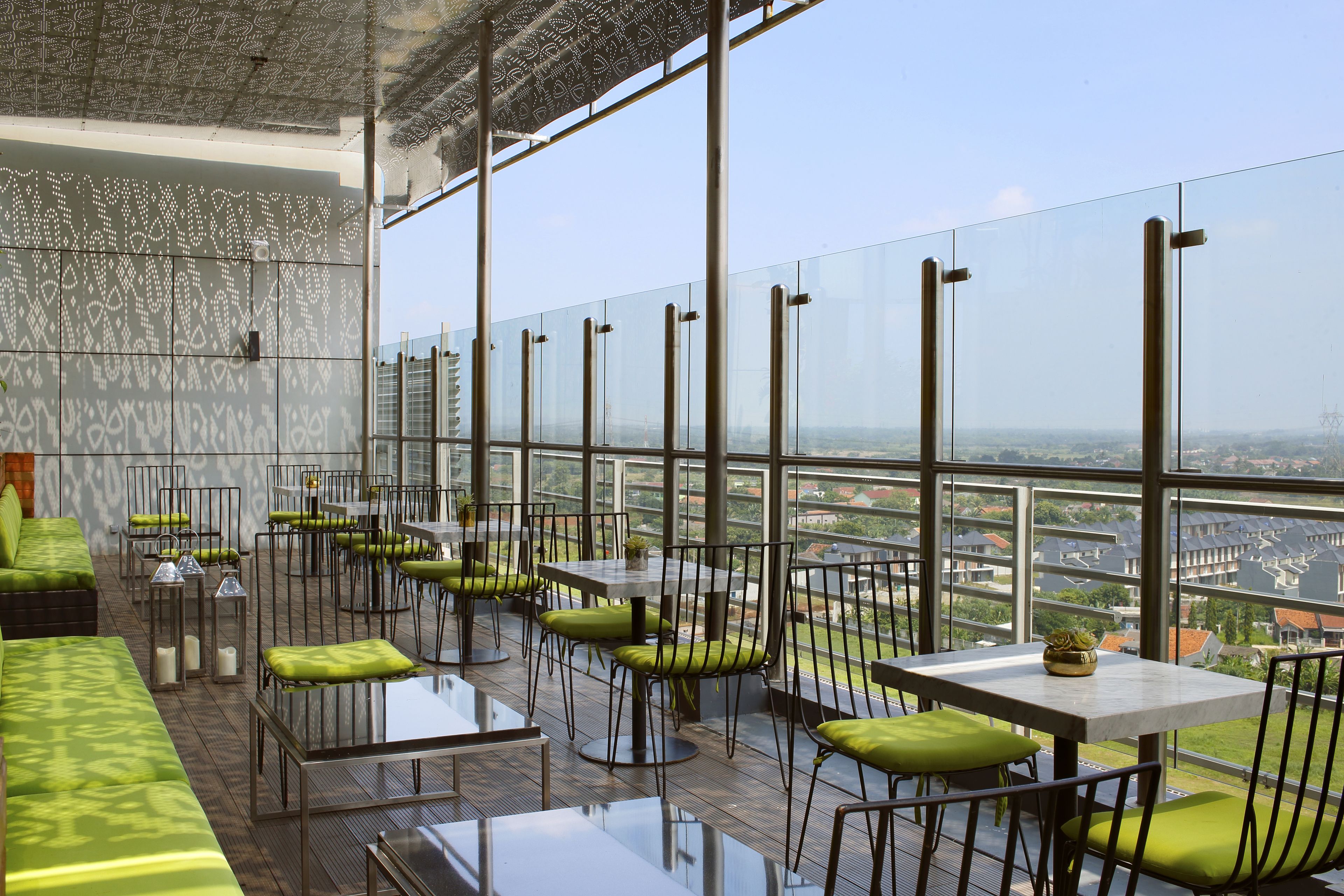 A modern restaurant with glass walls, green cushioned seating, and a city view.
